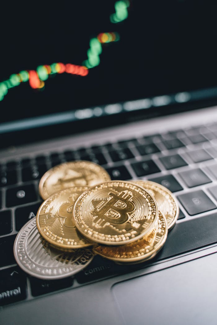 Stack of Bitcoin coins on a laptop keyboard with trading graph background, symbolizing cryptocurrency trading.
